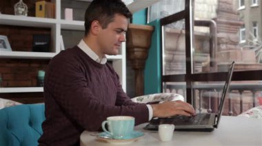 Kafede dizüstü üzerinde çalışmak için beyaz adam bitirme. Esmer adam kafede masada dizüstü kapanış. Sandalyeye kafesinde kendisini strecthing genç adam