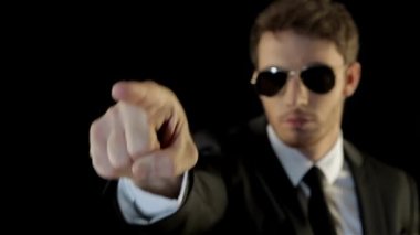 Beyaz adam siyah arka plan karşı izole onun işaret parmağı işaret güvenlik gibi giyinmiş. Esmer adam ileri onun işaret parmağı atma siyah paketindeki. Cool adam onun işaret eden havacı güneş gözlüğü