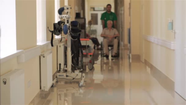 年轻的医生在医院推轮椅的病人 高级的白种人男子 坐在轮椅上 布鲁内特男军医牵他的手的轮椅的处理方法 — 图库视频影像