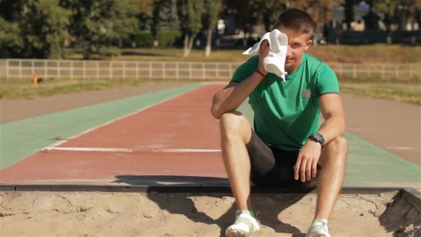 Молодой Атлет Вытирает Лицо Белым Полотенцем Кавказский Спортсмен Сидит Краю — стоковое видео