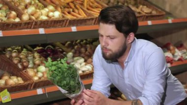 Süpermarkette fesleğen kokan çekici bir adam. Kafkas sakallı adam elinde bir demet fesleğen tutuyor. Alışveriş merkezinde fesleğen değerlendiren genç adam yakın çekim