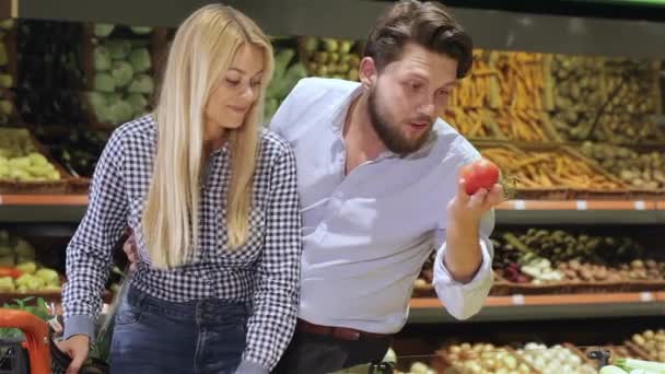 不错的夫妇在购物中心买西红柿 胡子的白种人男子从托盘里拿出一些樱桃番茄 迷人的金发女人把一些番茄放进手推车 — 图库视频影像