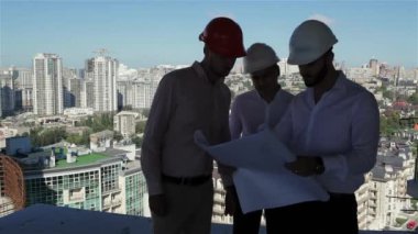 Üç erkek inşaatçılar inşaat aşamasında bulding projesini inceliyor. İnşaat aşamasındaki binada zeminin kenarında duran üç inşaat uzmanı. Erkek inşaatçılar görüntüleme