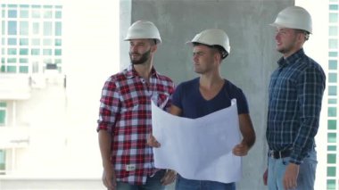 İnşaat halindeki binada poz veren şapkalı üç inşaatçı. İki inşaat işçisi damalı gömlekler giyerken, üçüncüsü mavi tişört giymiş. Üç ortasında Kafkas adam