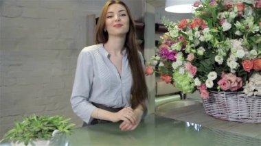 Genç kadın çiçekçi çiçekçi dükkanı çalışma masasında yaslanmış. Oldukça Kafkas kadın büyük rengarenk buket çiçek poz. Güzel kahverengi saçlı bakarak çekici kız