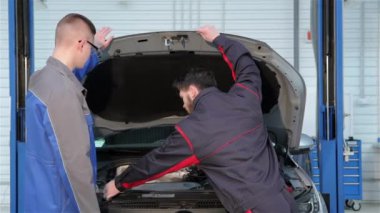İki genç Beyaz mekanik motor bölümü, araba servisi açın. Sakallı adam araba hood kaldırma. Onların başparmak yukarı kaldırarak iki otomotiv uzmanları