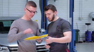 İstemci araba servisinde yapılan onarımların listesi imzalama. Sarışın beyaz adam onun kalçalarına ellerini koyarak. Sakallı makinist sarı seyir defteri istemciye vererek