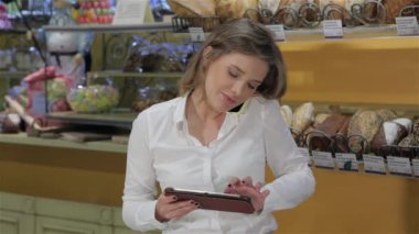 Genç bayan satıcı pastanede telefonla sipariş veriyor. Siparişi işlemek için dijital tablet kullanan beyaz bir kadın. Çekici kahverengi saçlı kadın dokunmatik ekranda yazı yazıyor.