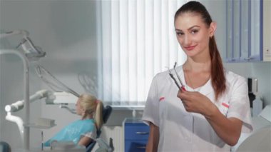 Diş hekimi kabine onun araçları gösteren genç diş hekimi. Çok kadın dişçi diş ayna ve sondalar tutarak. Kırmızı elma onu çerçevede gösterilen çekici brownhaired kadın