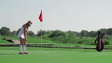 Düşük ihtimal olan çekici beyaz kadın golf adlı koymak için hazırlanıyor. Genç kadın golfçü flagstick duruyordu. Biraz top golf kulübü tarafından iterek oldukça ince kız
