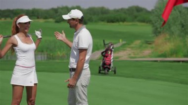 Çekici erkek golf eğitmeni kadın golf hakkında söylüyorum. Beyaz delikanlı aktif olarak ellerini tarafından el hareketi beyaz şapkalı. Kızıl saçlıya kadın Golf eğitmeni ile flört