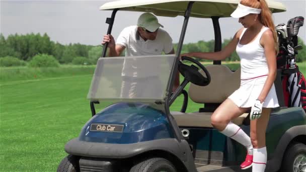 ゴルフカートに座っている若い白人男性と女性 かなり赤毛の女性ゴルファーがゴルフカートを運転しています 彼女の足でゴルフカートの加速器を押す魅力的なスリム女性 — ストック動画