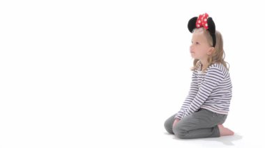 Küçük sarışın kız yere oturma. Kadın çocuk beyaz arka plan üzerinde izole Minnie Mouse Kostüm giymiş. Oldukça küçük kız dizlerinin üzerinde oturan