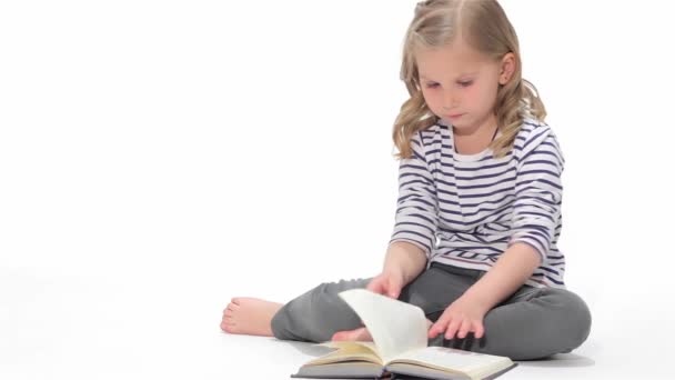 白人の子供が白い背景で隔離の本をざっとします 床に座って本を小さなブロンドの女の子 小さな子供の手でページを移動 — ストック動画