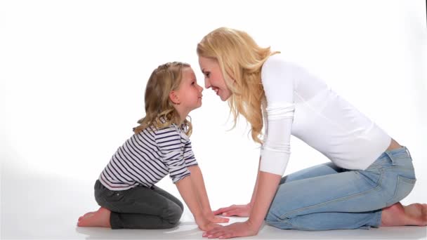 Female kid and her mother doing eskimo kiss isolated on white background. Blond mother and daughter rubbing nose to nose. Caucasian woman and little girl standing on their hands and knees
