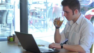Kafede dizüstü bilgisayar kullanan esmer adam. Laptop ve çay ile masada oturan genç adam. Beyaz adam kafede oturan penceresinin arka plan üzerinde beyaz gömlek giymiş