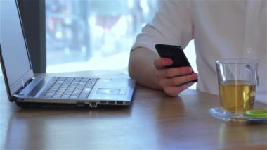 Genç adam onun smartphone kullanırken yeşil çay içme kapatın. Beyaz adam akıllı telefon şeffaf bir kupa kaldırma sırasında sağ elinde tutan. Her ikisi için de yazarak adam telefonda yaptıktan sonra eller.