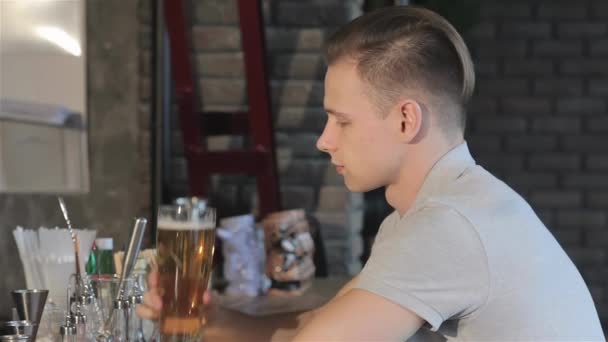バーで若い男がビールを飲んでいる バーカウンターに立つ白人男性 ブロンドの男はビールを口に持ってくる — ストック動画