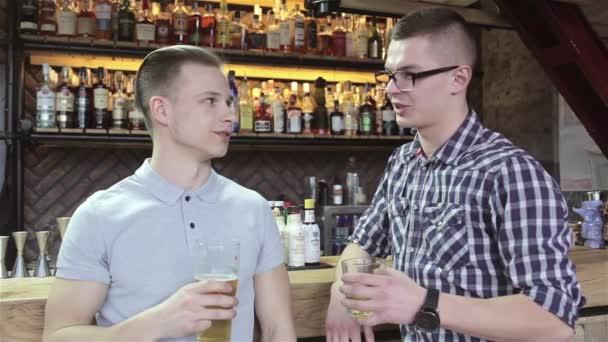 两个现代人在酒吧喝酒 金发男子穿着白色T恤 布鲁内特男子穿着格子T恤 他们的眼镜闪烁 年轻的白人男子与眼镜的男人 — 图库视频影像