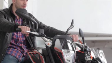 Siyah motosikletgidon tutarak danışman yakın. Motosikletin gidonunu sağa çeviren genç adam. Siyah spor motosiklet danışmanı kameraya gülümseyerek