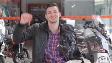 Elinde motosiklet anahtarlarını sallayan danışman. Motosiklet bayiinde bir erkek satıcının yakını. Beyaz motosiklet üzerinde oturan gülümseyen esmer adam