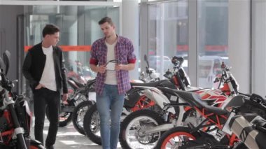 Satış motosiklet salonu ile müşteri ile yürüyüş. Danışman ve alıcı çapraz motosiklet satır yakınında durdurmak. Satıcı ve müşteri el sıkışırken