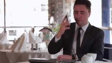 Restoranda, kafede, kafede iş yemeği. Rahat giyimli genç işadamı bir kafe, restoran, kafede bir masada yemek. Erkek bir tablet kullanır.