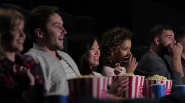 Sinema, eğlence ve insan kavramı - mutlu arkadaşlar tiyatroda film izlerken. Sinemada film izlerken patlamış mısır yiyen ve soda içen çift ve diğer insanlar.