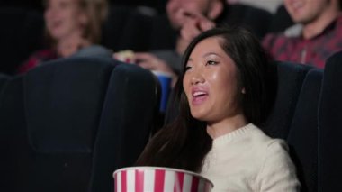 Asyalı kız bir melodram sırasında duygularını gösterir. Sinema, eğlence ve insan kavramı - mutlu arkadaşlar tiyatroda film izlerken. Çift ve diğer insanlar patlamış mısır yemek ve soda içerken