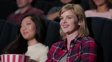 Bir melodram izlerken Asya kız arkadaşı fısıldıyor. Sinema, eğlence ve insan kavramı - mutlu arkadaşlar tiyatroda film izlerken. Çift ve diğer insanlar patlamış mısır yiyor ve