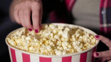 Bir kova patlamış mısır ve kızın elini kapat. Film izlerken patlamış mısır çiğniyor. Sinema, eğlence ve insan kavramı - mutlu arkadaşlar tiyatroda film izlerken. Çift ve diğer kişiler