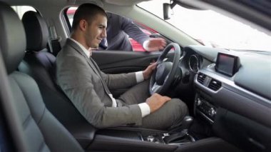 Arabada oturan genç adam. Otomatik iş, araba Satılık, teknoloji ve insan kavramı - auto göstermek ya da salon araba satıcısı ile mutlu erkek. Bir satıcı motor gösterisi ile genç adam.