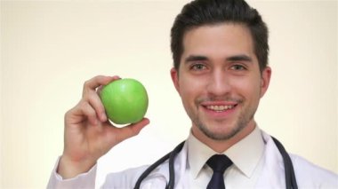 Yeşil elma ile gülümseyen erkek doktor. Şırınga, hap, fanendoskop, röntgen, pano, tıbbi maske, elma, şeker, çocuklar için yumuşak oyuncaklar ile beyaz bir tıbbi elbise li beyaz bir hemşire veya doktor erkek