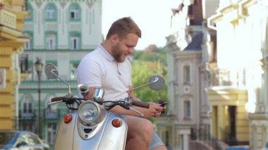 iyi konuşma ile arkadaş. scooter üzerinde oturan ve cep telefonda konuşurken neşeli genç adam