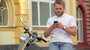 Scooter üzerinde otururken cep telefonunu kullanan genç modern adam portresi