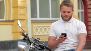 Scooter üzerinde oturan ve telefon kullanarak genç yakışıklı şık adam