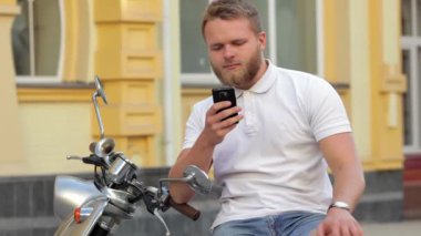 Genç motosiklet içinde telefon ile oturan adam sakallı. Telefon ile motosiklet içinde oturan genç adam