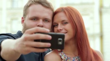 Oldukça genç bir çift bir şehir bankta otururken bir selfie ile onların akıllı telefon alarak. Güneşli bir günde bir selfie bir parkta bir akıllı telefon ile kentsel bir arka plan ile çekim Çift