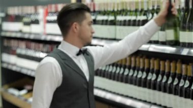 Doğru şarap seçimi. Kendine güvenen erkek sommelier şarap şişe şarap raf yakınındaki dururken incelenmesi