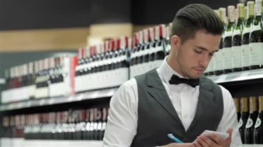Kendine güvenen sommelier. Bir şey de onun not defteri yazma ve şarap şişeleri seyir kendine güvenen genç sommelier yan görünüm