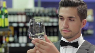 Büyük renk. Yelek ve papyon kırmızı şarap kadehinin tutarak ve şarap raf önünde ayakta iken inceleyerek kendine güvenen genç adam