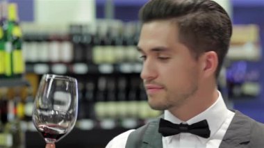 Bu şarap mükemmel. Kendine güvenen erkek sommelier şarap kadehinin seyir ve arka planda şarap raf ile tahta masada yaslanmış iken incelenmesi