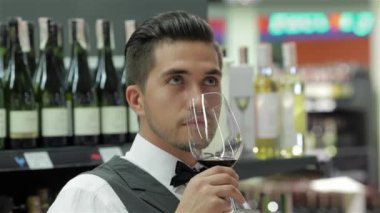 Kendinden emin ve deneyimli sommelier. Kendine güvenen genç adam yelek ve papyon ile kırmızı şarap şarap bardağını tutan ve kokulu Close-Up