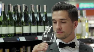 Sommelier şarap incelenmesi. Kendine güvenen erkek sommelier şarap kokulu ve arka planda şarap raf ile tahta masada yaslanmış iken inceleyerek görüntüsünü