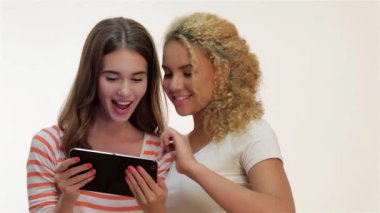 Beyaz arka planda iki kadın tablet bilgisayarı tutuyor. Dokunmatik ekran üzerinde çalışıyorum. Gülümseyen, kahverengi saçlı, kızıl saçlı bir kadın. Beyaz arka planda iki kız.