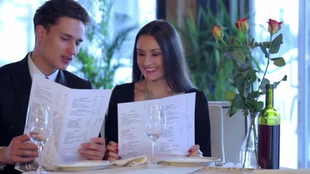 选择的菜肴 餐厅里的浪漫晚餐年轻夫妇在参观餐馆菜单时 手里拿着一份菜单 选择一道菜 面带微笑地看着菜单 浪漫的相遇 — 图库视频影像