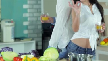 Çift, arka arkaya holding portakal suyu ayakta kız Tamam gösterir. Genç gülümseyen arkadaşlar kesilmiş sebzeler ise mutfakta yemek. Birlikte yemek yiyecek.