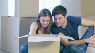 Evime taşınmaya sevinç. Bir çift holding kutusu elinde sevgi dolu ve kutusunda kutuları arasında boş bir daire içinde kanepede oturan aşık genç ve güzel bir çift süre seyir