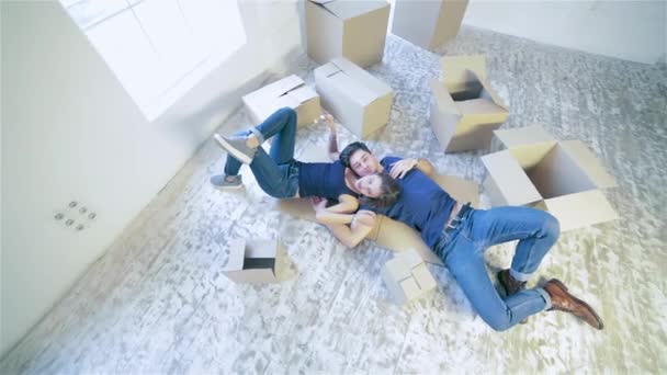 新しい家を修理 男ながら空のアパートのボックスの中で床に横たわる女を抱きしめることで床に横にカップルの女の子と男 — ストック動画