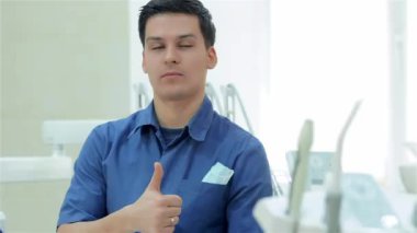 Başarılı bir dişçi portresi. Gülümseyen ve başparmak kameraya, hastanın diş donanımları arasında çekmeden önce göstermek yukarıya diş hekimi